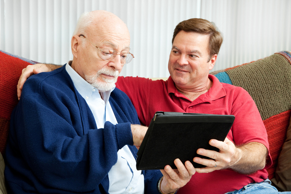 Younger man assisting older man to use an ipad