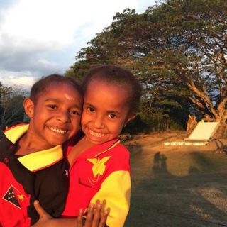 Photographed at sunset, two smiling schoolgirls hug infront of the slide built at their school