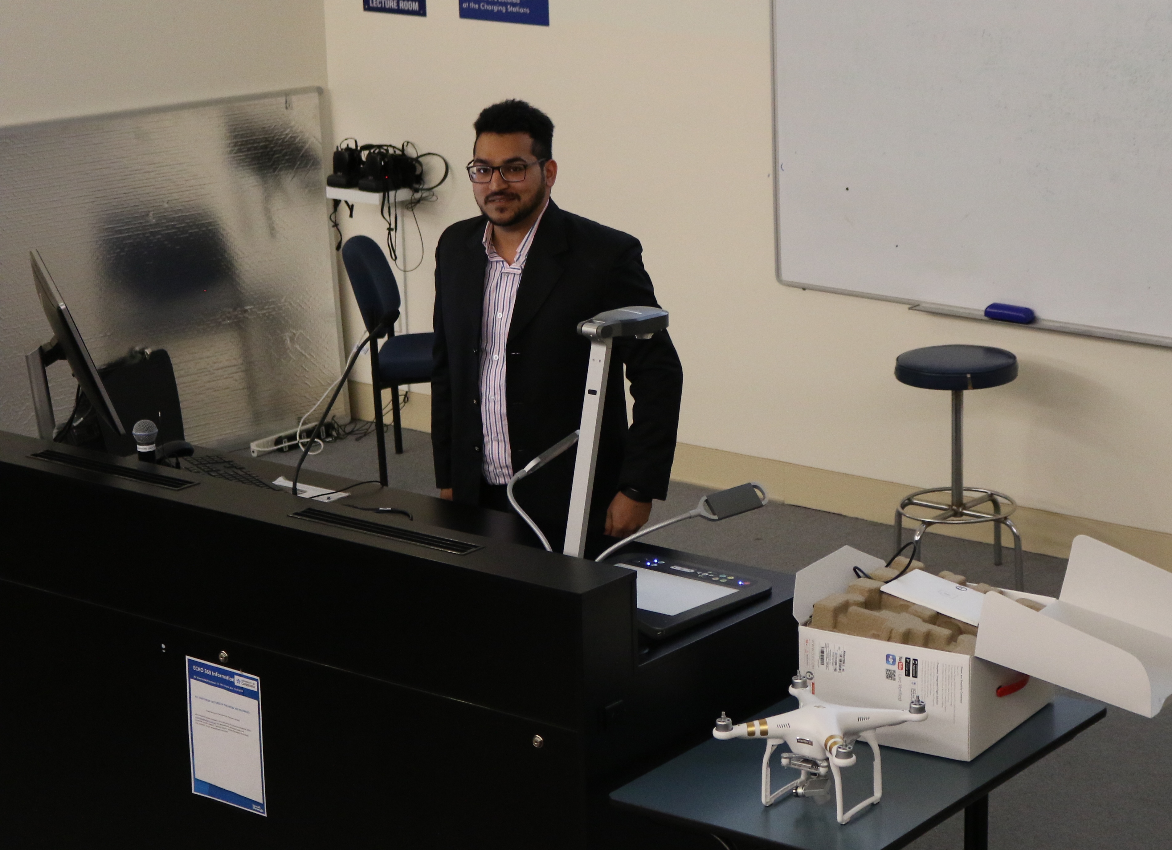 Mohammed Nizamuddin Rizwan delivers his WRS Presentation, one of the drones he used in his research sits on the desk
