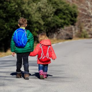 Two children wearing winter jackets are walking along a road