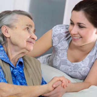 An older woman holds the hand of a younger carer