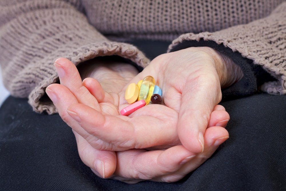 An older person holds a selection of pills and vitamins in their hands