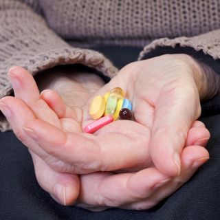 An older person holds a selection of pills and vitamins in their hands