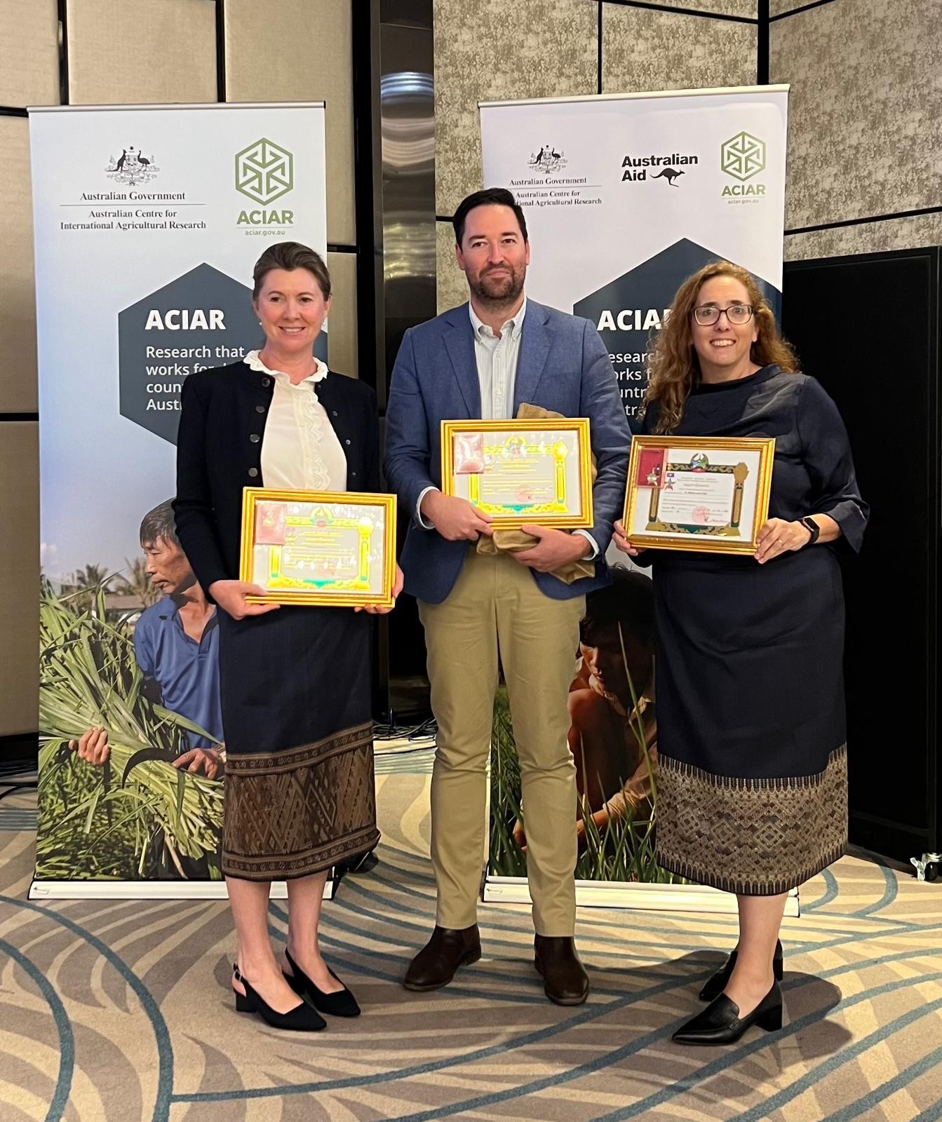 Three people stand side-by-side holding certificates