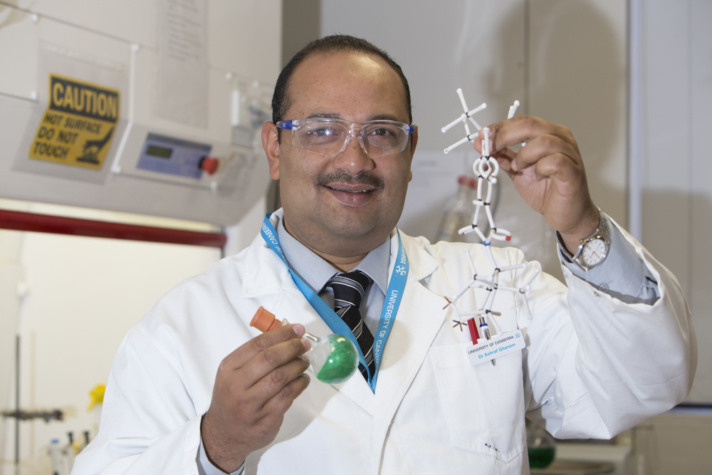 Dr Ashraf Ghanem in his laboratory, holding a model of the catalyst molecule and a round-bottomed flask of the catalyst.