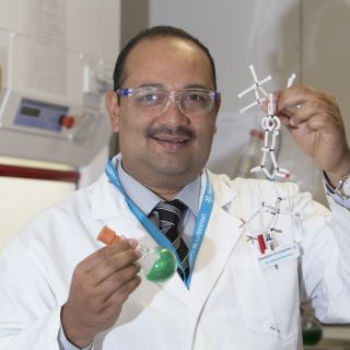 Dr Ashraf Ghanem in his laboratory, holding a model of the catalyst molecule and a round-bottomed flask of the catalyst.