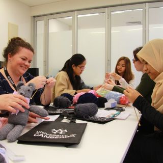 Members of the Knitting project group relax and knit around a table where completed Trauma Teddies are on show