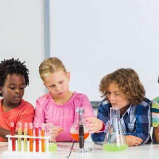 A group of young students sit at a school table with various science equipment