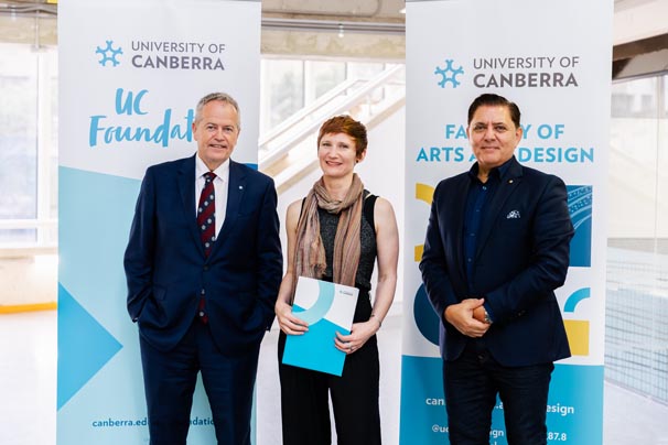 Sarah Brown (middle) holding her scholarship certificate,with Vice-Chancellor Bill Shorten on the left and UC Council member Medy Hassan on the right standing in front of University of Canberra banners