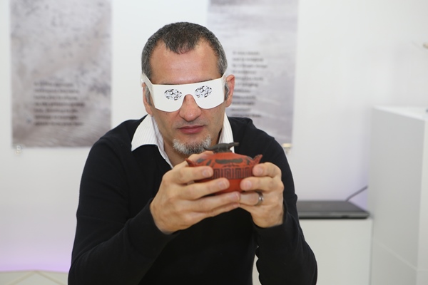 PhD Student Beaux Guarini wears a pair of paper spectacles which simulate a vision impairment while holding his 3D-printed sugarbowl.