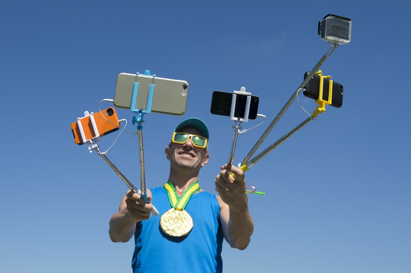 An athlete wearing a gold medal holds several smartphones on 'selfie-sticks'