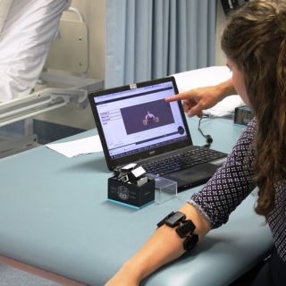 Research student Amy Webb sits at a desk using the Myo armband while watching an app on a laptop