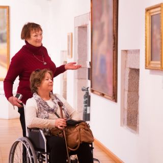 Two women, one using a wheelchair, visit an art gallery