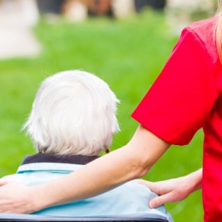 An older person sits while a younger carer rests a comforting hand on their shoulder