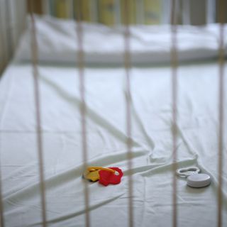 An empty cot with a small baby's rattle
