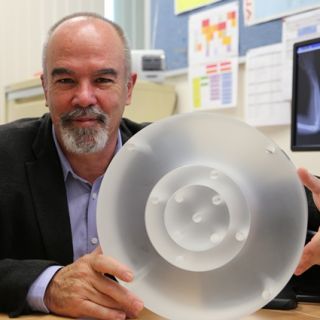 Professor Rob Davidson at his desk resting his arm on a large translucent perspex cylinder
