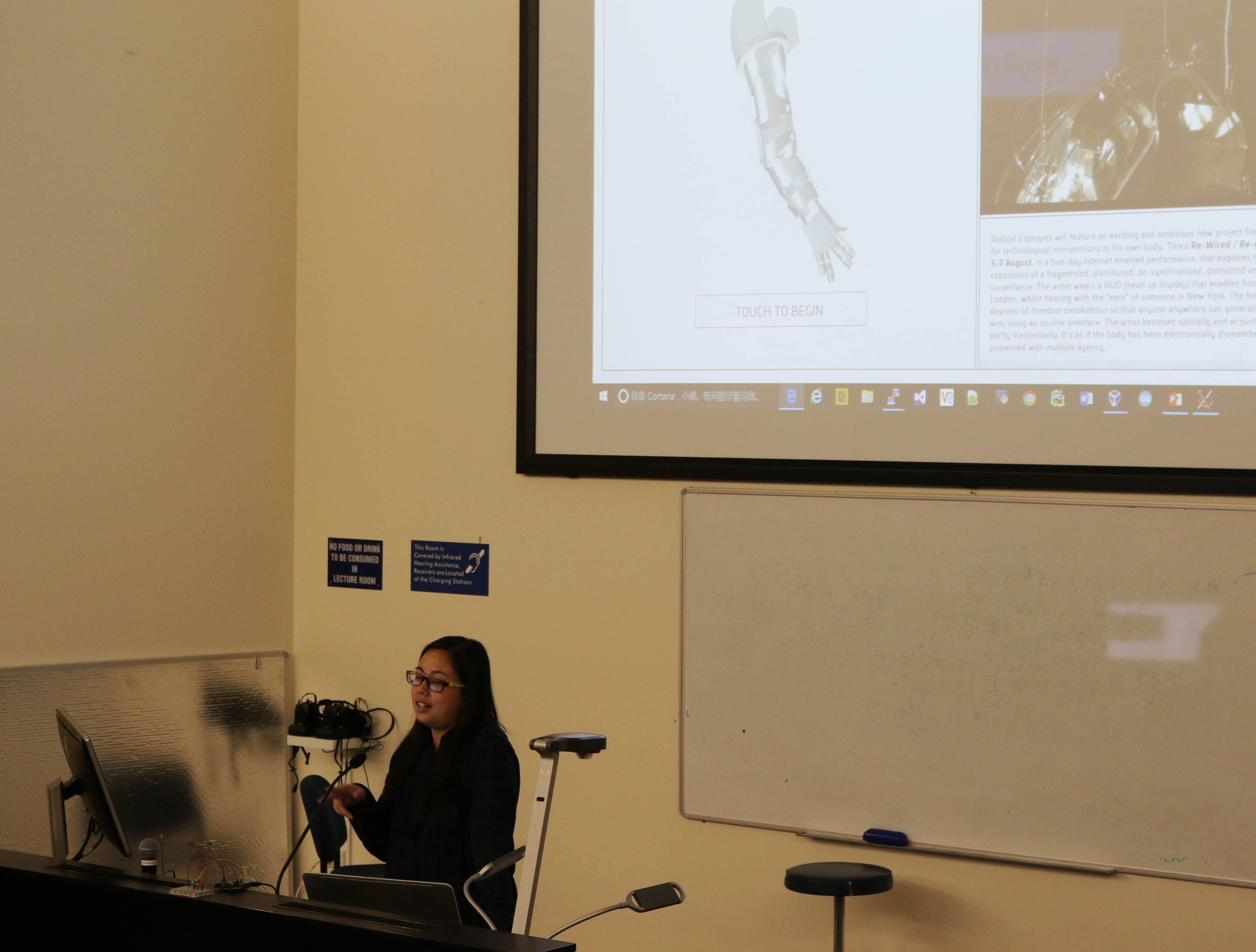 Ivy Zhu delivers her final presentation in a UC lecture theatre, with a projector showing her link-up with a performance artist
