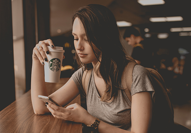 Young woman drinking coffee and looking at her mobile phone