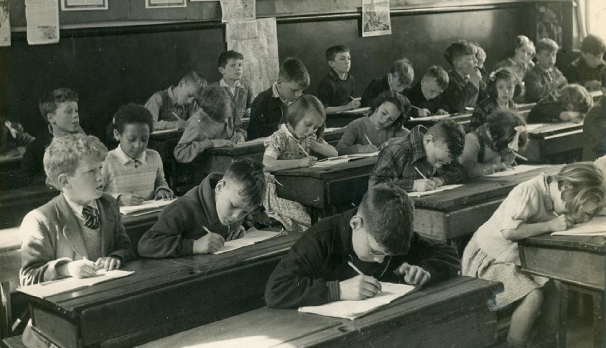 Black and white historical photo of children writing at desks in school