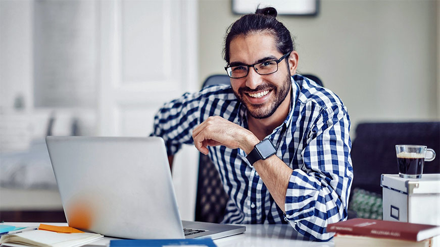 Smiling man sitting with a laptop studying a Master of Creative Industries.