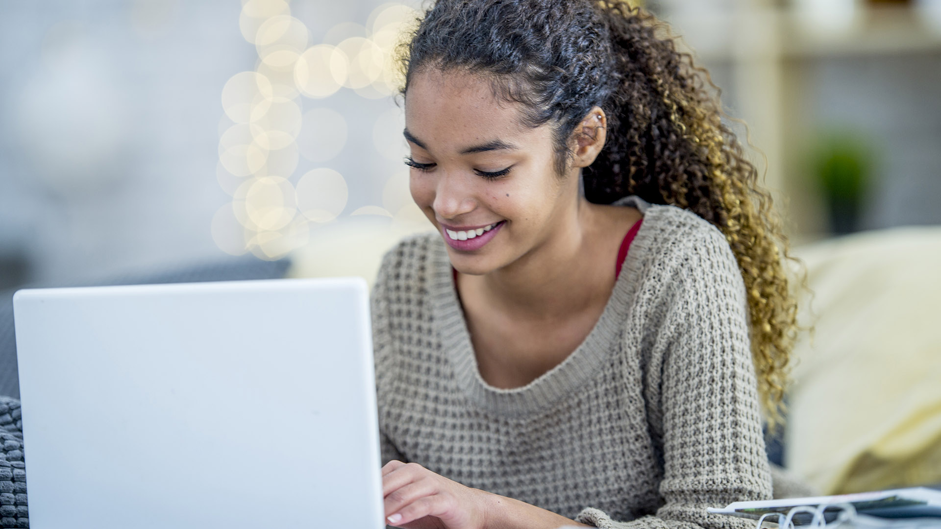 A young female student happily smiling and typing on her laptop.